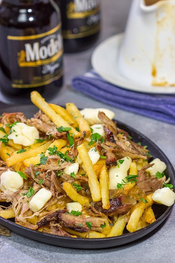 El norte se encuentra con el sur en esta sabrosa receta de poutine de puerco desmenuzado.  ¡Las papas fritas cubiertas con cuajada de queso, salsa marrón y cerdo desmenuzado ahumado a fuego lento son un delicioso aperitivo o comida!